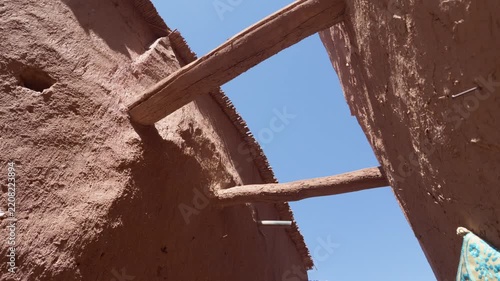 Traditional mudbrick architecture of a berber kasbah in morocco with wooden beams supporting the walls against a clear blue sky, showing local handicrafts for sale