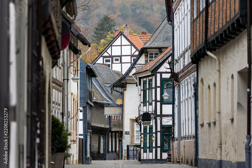 Scenic Goslar rooftops frame historic street with half timbered houses, slate facades and museum sign. Soft autumn tones and hazy hills create tranquil heritage mood in charming old town center