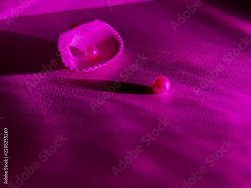Seashell with two pearls in vivid pink magenta light and dramatic shadows