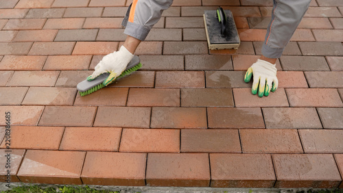 Construction worker sweeping sand into joints of new red brick pavers