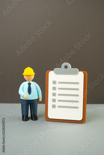 Official in a yellow hard hat with a paper clipboard. Inspections and tests. Audits and occupational safety standards. Construction compliance, workplace regulations and quality control.