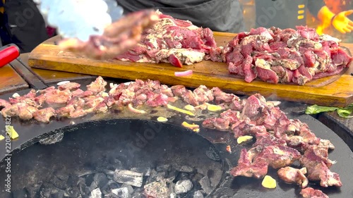 Outdoor street food chef grilling seasoned marinated meat slices on a hot circular iron plate over burning charcoal, filled with smoky savory flavor and rustic barbecue vibe. 4K video.