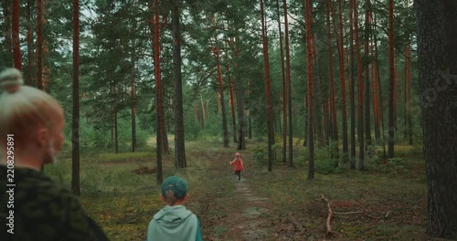 Mother walks along a forest trail with her three children during a family nature walk. One girl runs ahead while the mother and two other children follow through the pine forest. High quality 4k