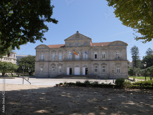 View of the Deputacion Provincial de Pontevedra Pazo Provincial, a grand neoclassical stone building with flags displayed on the facade, situated in a park in Pontevedra, Pontevedra, Spain.