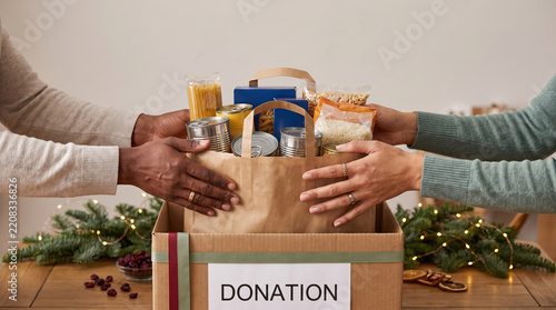 Two people handing a bag of food donations into a donation box