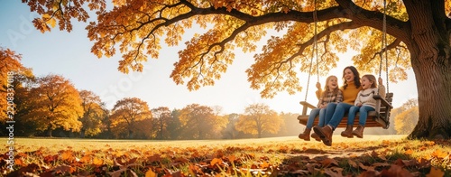 Happy mother, two young daughters ride wooden swing under big autumn tree. Smiling family enjoys leisure time in public park. Girls laugh swinging on playground equipment during sunny fall season in