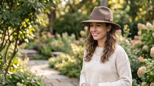 Young woman smiling while wearing a fashionable fedora hat in a garden  
