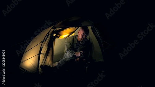 A man cooking food inside a tent at night 