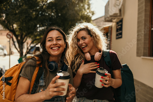 Young women friends traveling laughing holding coffee cups
