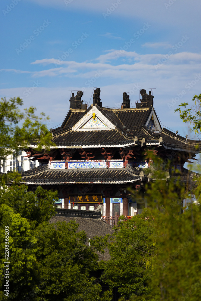 Fototapeta premium Traditional Chinese Pavilion with Curved Roofs and Green Trees Against Blue Sky
