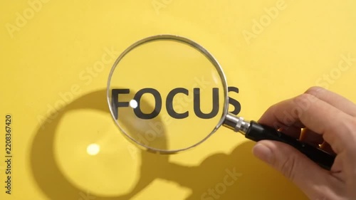 Hand holding magnifying glass focusing on word 'FOCUS' against bright yellow background - concentration concept