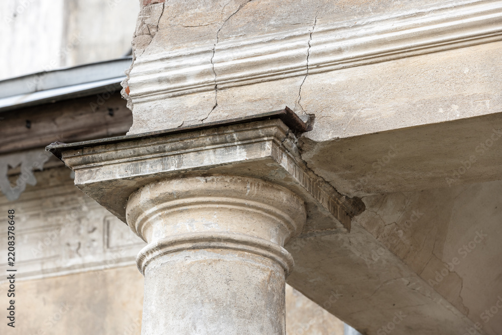 Obraz premium Close-up of a weathered classical stone column and entablature showing cracked plaster, aged masonry and architectural detail on a historic facade conveying decay, texture and heritage