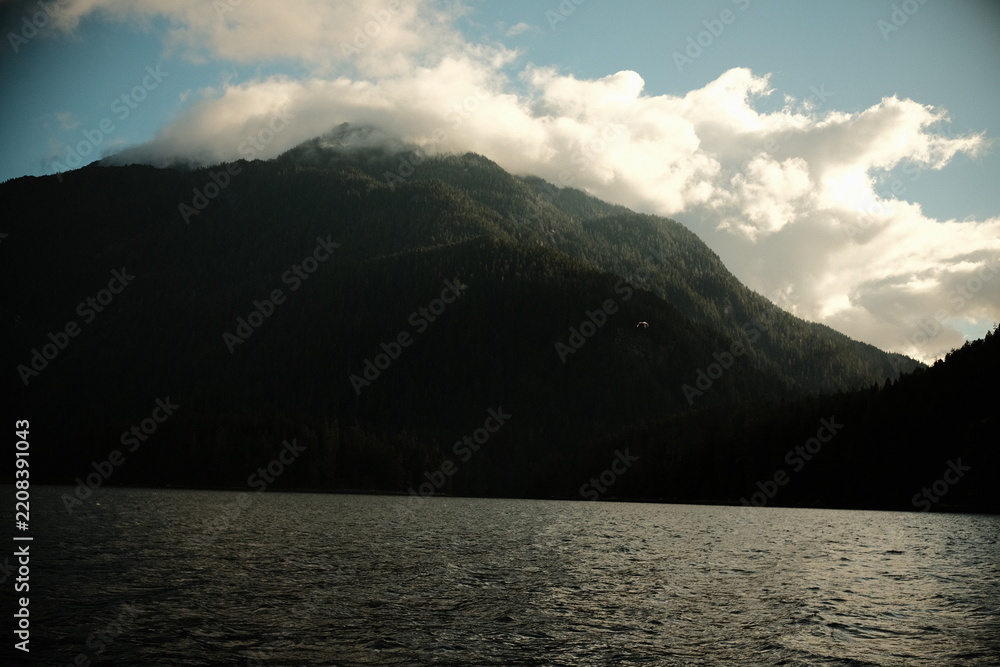 Obraz premium Clouds wrapping a dark mountain above a wide lake