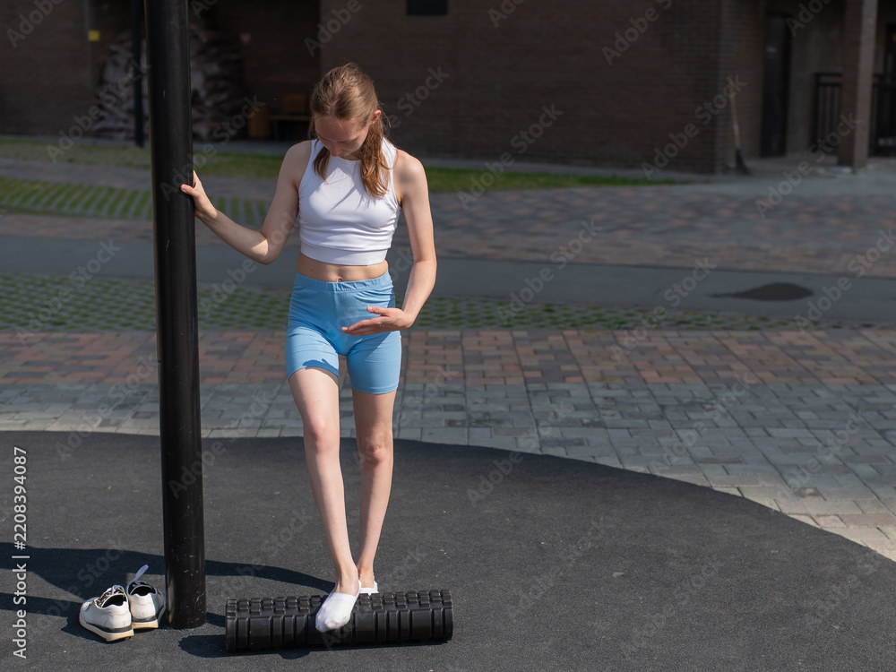 Obraz premium A Caucasian woman stretches her feet with a foam roller at a sports ground.