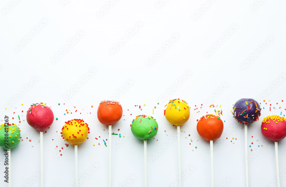 Fototapeta premium Colorful cake pops with sprinkles on white background, flat lay. Space for text