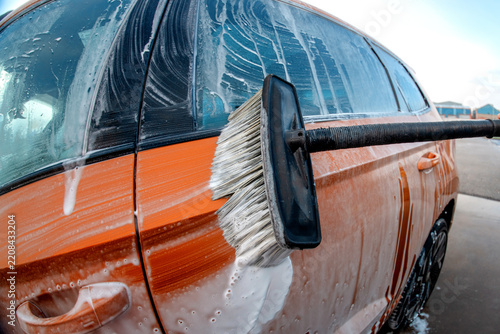Car washing with a brush on a sunny day near a car wash station