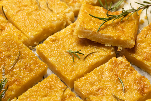 Close up of traditional Italian chickpea farinata baked in the oven and cut into square pieces with fresh rosemary. Vegan and vegetarian dish.