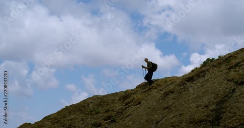 Man with a backpack descending from the summit against the backdrop of the sky.