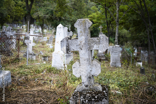 Old weathered stone cross in an overgrown cemetery. Close up of a mossy gravestone in an abandoned graveyard. Historic christian monument