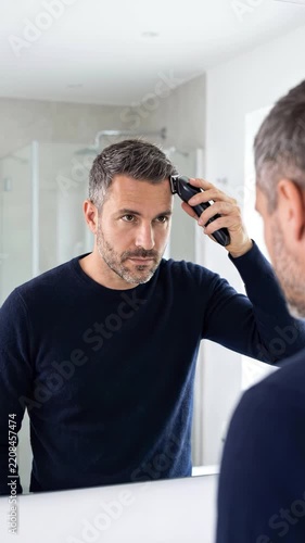 Man trimming hair with electric trimmer in front of bathroom mirror