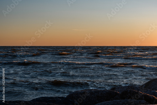 Fotografie Choppy sea waves during warm sunset dusk with coastal rocks in the foreground at Baltic Sea