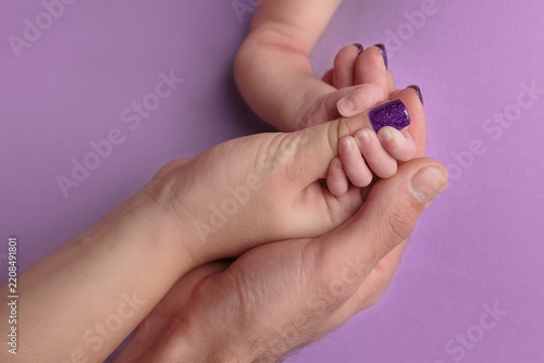 Adult Hand Holding Baby Hand on Purple Background