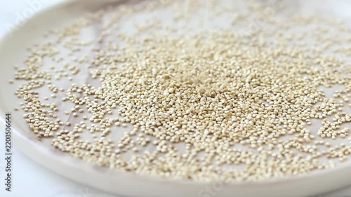 Raw quinoa seeds are falling into a plate.