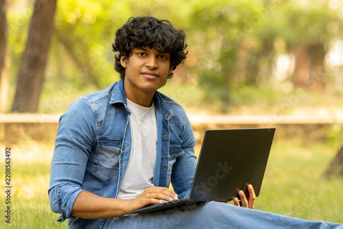 Indian college male student studying at park while using laptop
