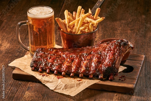 Barbecue pork ribs with french fries and beer on a wooden board with copy space for menu design
