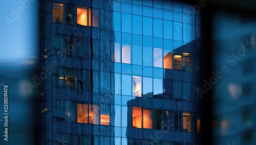 Evening view of a modern office building glass facade with illuminated windows.