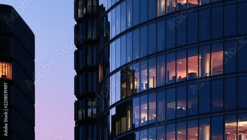 Modern glass office building exterior at dusk with glowing windows.