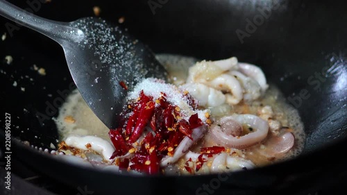 4K Chef pouring white sugar seasoning into a hot wok with squid rings chilies and garlic, cooking process for spicy Thai stir-fried squid with holy basil concept.
