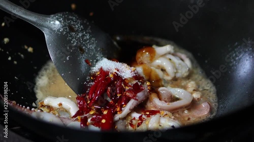 4K Chef adding fresh holy basil leaves into a hot wok with squid rings chilies and garlic, final step of cooking Thai stir-fried squid with basil.