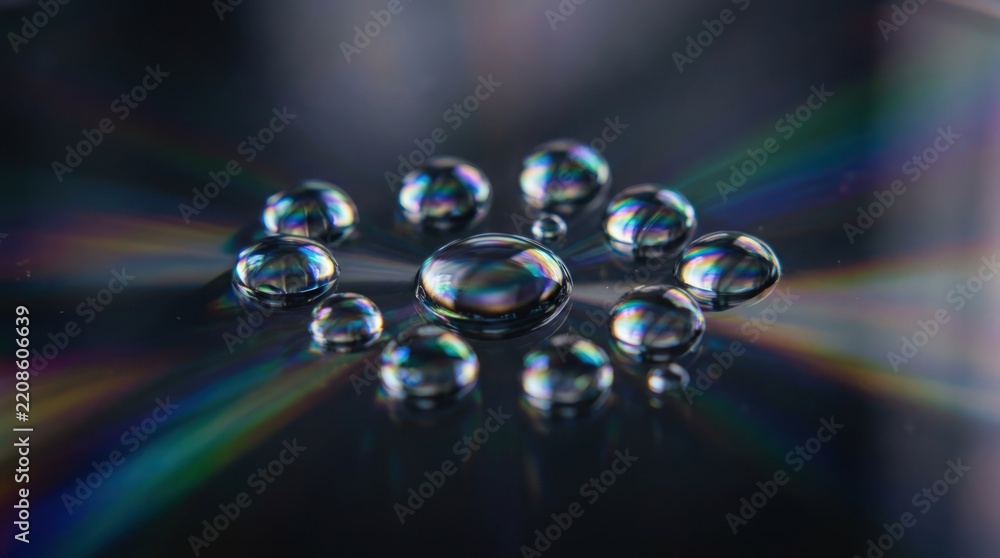 Obraz premium Water droplets on a dark reflective surface with rainbow light refractions