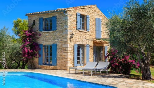 A charming stone villa with blue shutters and a swimming pool.