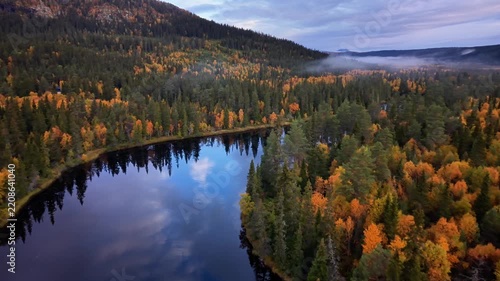 Aerial view of Ljusnan river winding through a dense forest with vibrant autumn foliage and calm water reflections in Funasdalen, Jamtland County, Sweden.