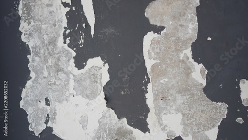 Weathered, peeling, and crumbling dark gray concrete wall texture with flaking white paint, suitable for backgrounds or wallpapers.