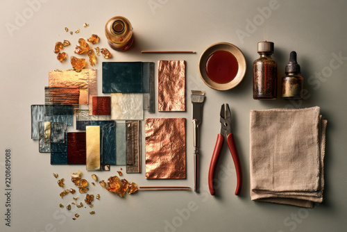 Artisan metalwork flat lay with copper sheets, patina samples, amber fragments, pliers, brushes, bottles and cloth arranged as a creative craft collection.