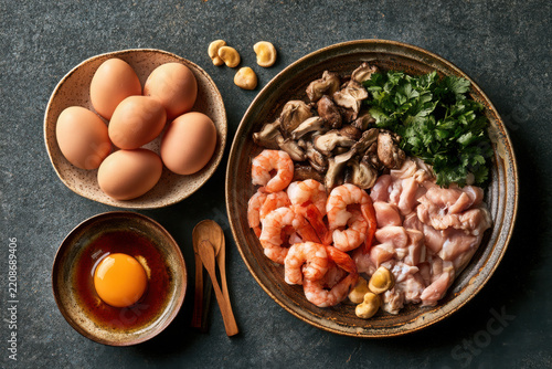 Asian inspired ingredient flat lay with egg, prawn, chicken, mushroom, parsley and nut arranged in ceramic bowls for a fresh gourmet meal preparation.