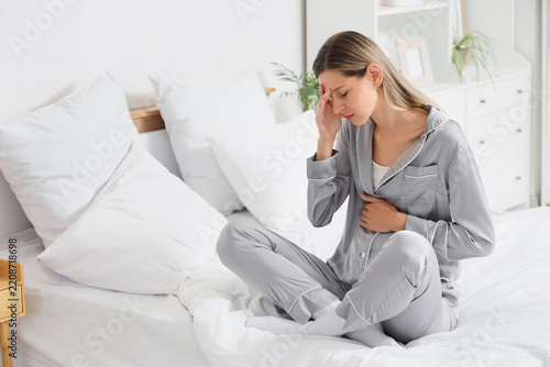 Health issues and morning sickness, woman in pajamas sitting on bed feeling n...