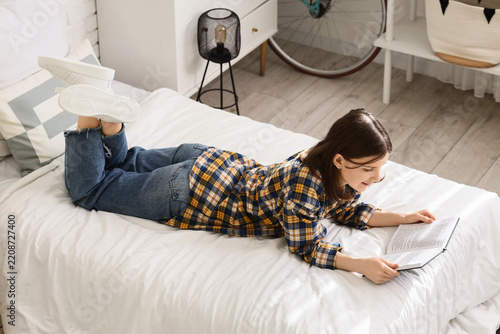 Self-care and leisure time, young woman reading a book while lying on a bed i...