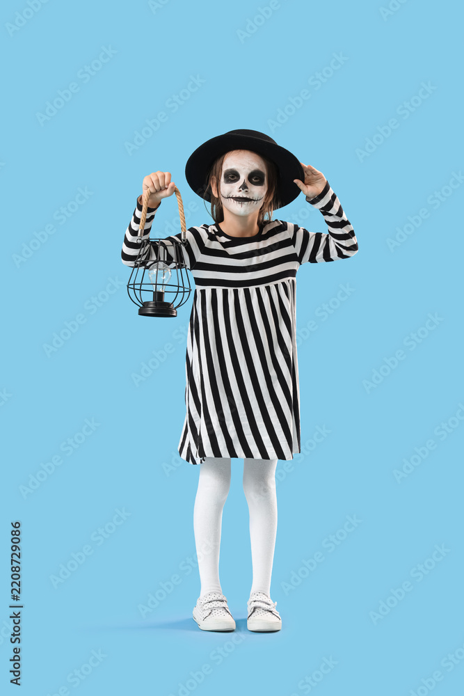 Fototapeta premium Halloween celebration and childhood imagination, little girl in skeleton makeup and striped dress holding a vintage lantern on a blue background