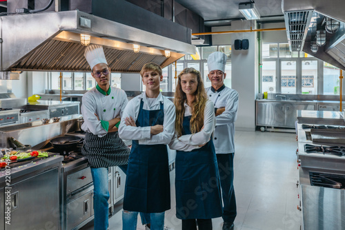 Team portrait of Asian chefs and teen culinary interns with arms crossed in a professional kitchen