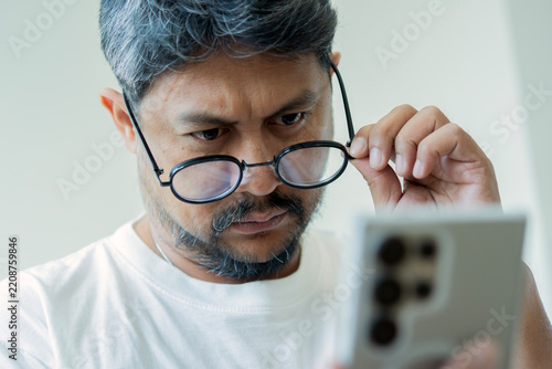 Close-up of an adult man peering over his eyeglasses while llling at his mobile phone screen