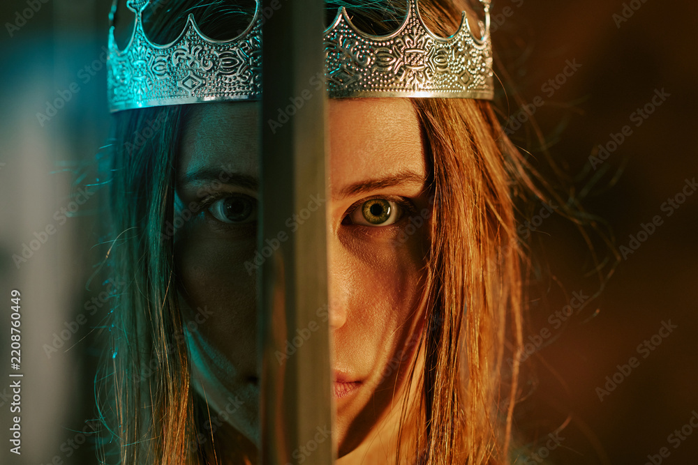 Obraz premium Portrait of young adult Caucasian woman wearing silver crown and holding sword in front of face. Concept representing power, leadership, and strength for fantasy branding, close up shot