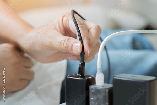Hand plugging a black charging cable into a power adapter adapter socket