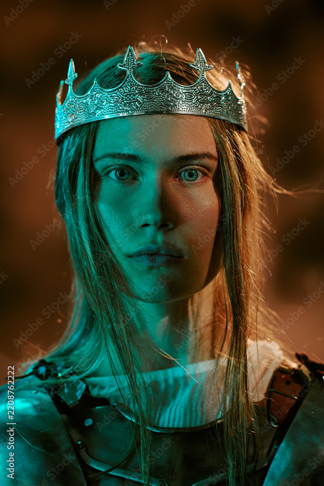 Obraz premium Portrait of young adult Caucasian woman wearing crown and armor, looking at camera. Concept of leadership, power and strength for gaming, fantasy book covers, vertical