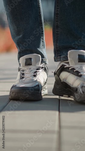 Close up of person walking showing white sneakers and blue jeans in motion. focus remains on lower legs as they move along outdoor path with soft lighting highlighting texture details