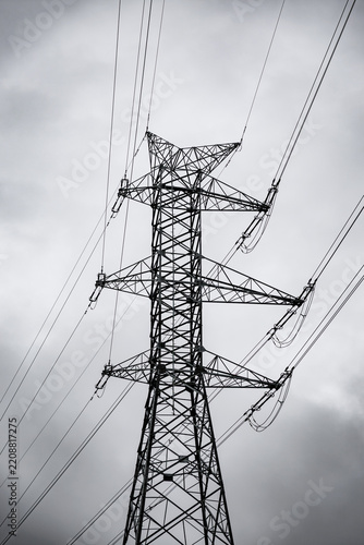 Tall electricity transmission tower and power lines silhouetted against a dramatic overcast sky, creating a stark industrial atmosphere with ample copy space
