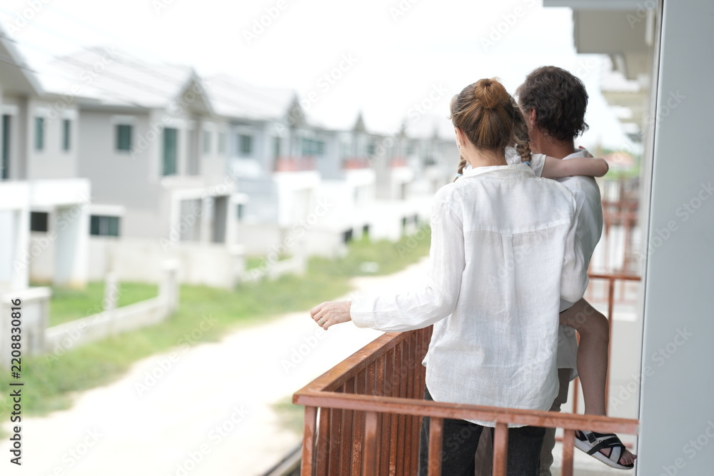 Fototapeta premium Happy young family with little daughter enjoy the view of the growing suburb from their balcony on the balcony of their new house overlooking the residential estate, shallow depth of field